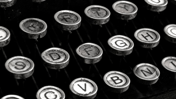 Close-up em preto e branco de teclas metálicas de uma máquina de escrever antiga, com várias letras visíveis e fundo escuro desfocado.